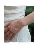 Colocho Bracelet worn on a model's wrist against a white dress, a solid 18k gold twisted chain bracelet. Tarnish-resistant and made for everyday wear — Maya & Mason handcrafted fine jewellery.