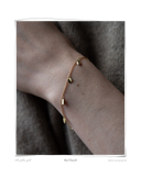 Curl Bracelet worn on a model's wrist against a neutral gray fabric background, a solid 18k yellow gold chain bracelet featuring eight signature curl charms. Tarnish-resistant and made for everyday wear — Maya & Mason handcrafted fine jewellery.